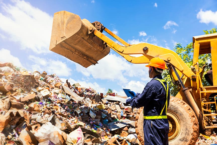 Crane operator. The engineer is controlling the loader to get the iron to recycle. Worker standing in metal landfill outdoors.