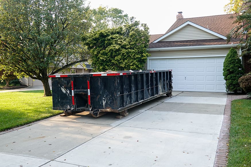 Long blue dumpster full of wood and other debris in the driveway in front of a house in the suburbs that is being renovated